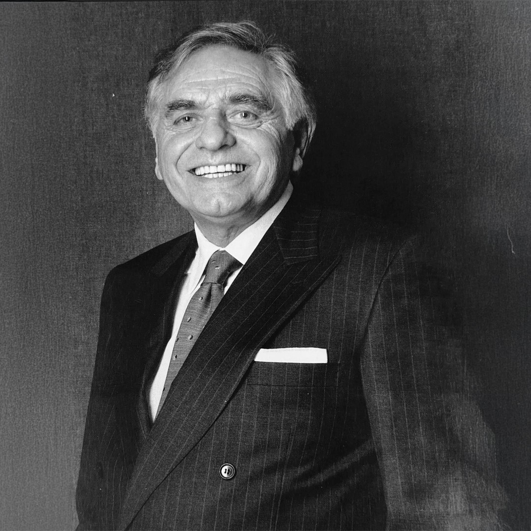 Retrato en blanco y negro de un hombre mayor sonriente con traje de rayas, corbata de puntos y pañuelo de bolsillo, f...