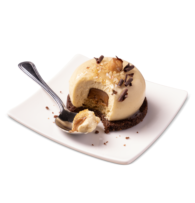 Postre en forma de cúpula de mousse de caramelo sobre base de galleta de chocolate, con avellanas y virutas de chocol...