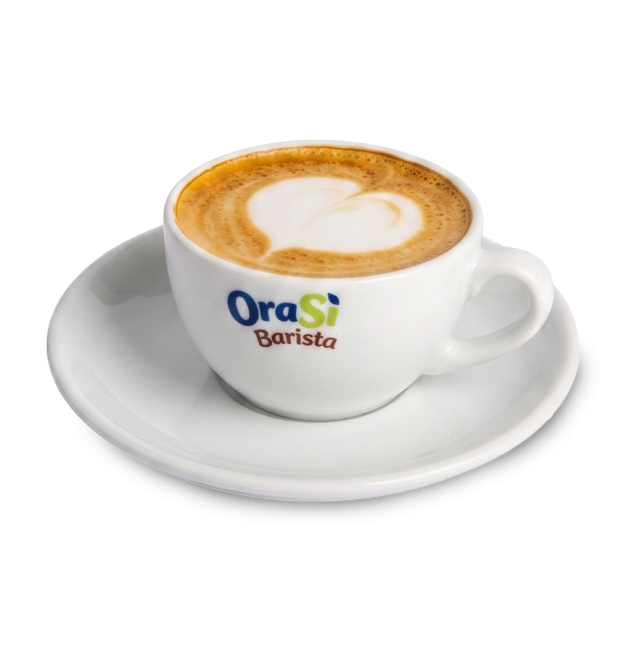 Taza blanca de capuchino con arte latte en forma de corazón, etiqueta "OraSì Barista", en plato a juego, fondo blanco