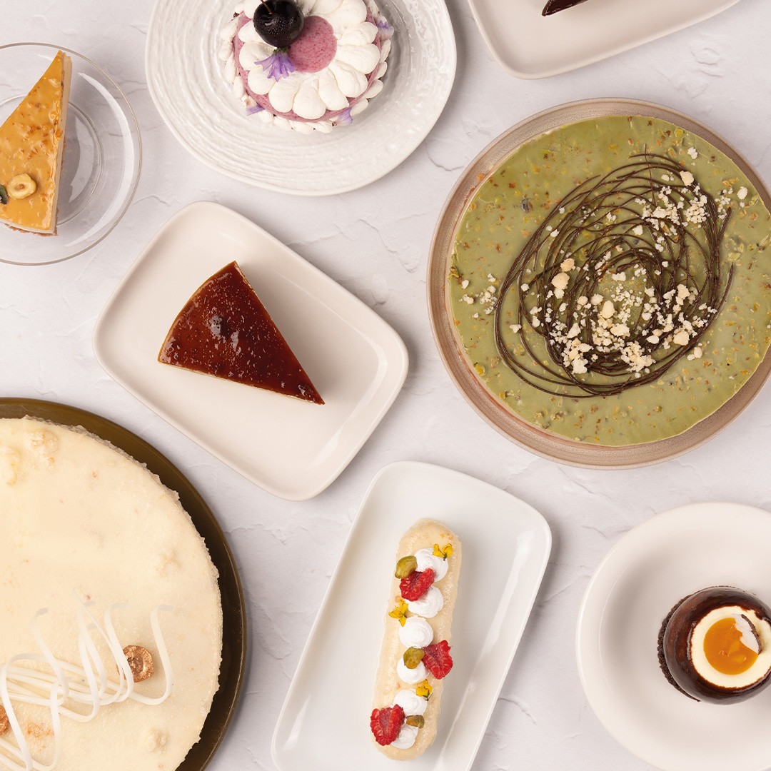 Vista superior de postres variados: cheesecake, flan, tarta de pistacho, éclair y mousse de chocolate en vasitos