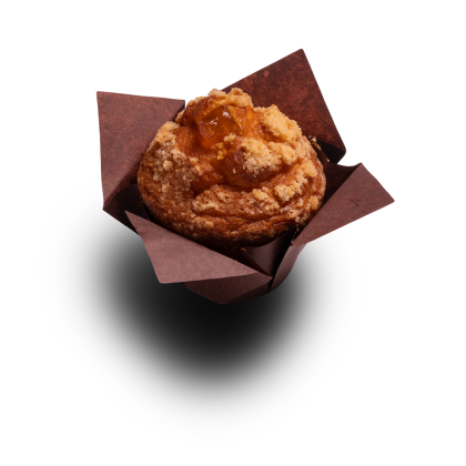 Muffin dorado cubierto con streusel y relleno de fruta, envuelto en papel marrón, sobre fondo blanco.