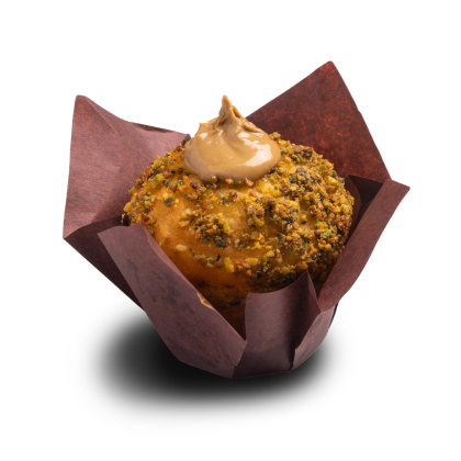 Muffin cubierto de pistacho triturado, con un remolino de glaseado de caramelo, en cápsula tulipán marrón.