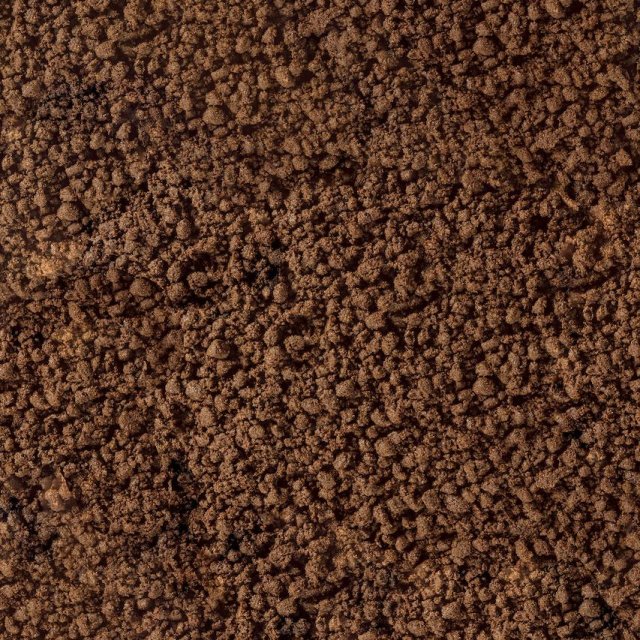 Primer plano de tierra suelta marrón o posos de café con textura gruesa y granulada llenando el encuadre.