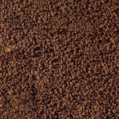 Primer plano de tierra suelta marrón o posos de café con textura gruesa y granulada llenando el encuadre.