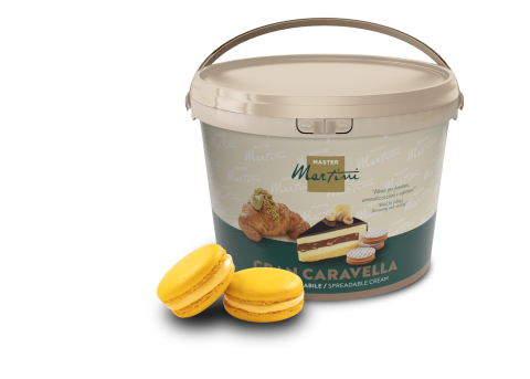 Cubo beige de crema untable Master Martini Gran Caravella junto a dos macarons amarillos y un pastel relleno.