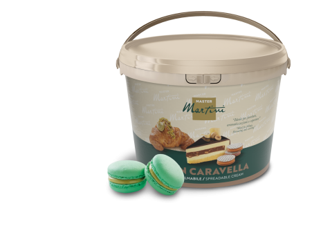 Tarrina beige de crema para untar Master Martini con imágenes de repostería, junto a dos macarons de pistacho verdes.