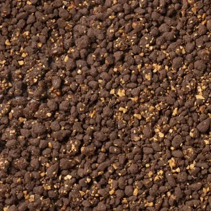 Primer plano de una mezcla marrón oscuro desmenuzable con frutos secos picados, con textura de crumble de chocolate o...