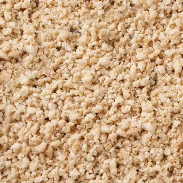Primer plano de gránulos beige claro desmenuzables con textura gruesa tipo migas que cubren todo el encuadre
